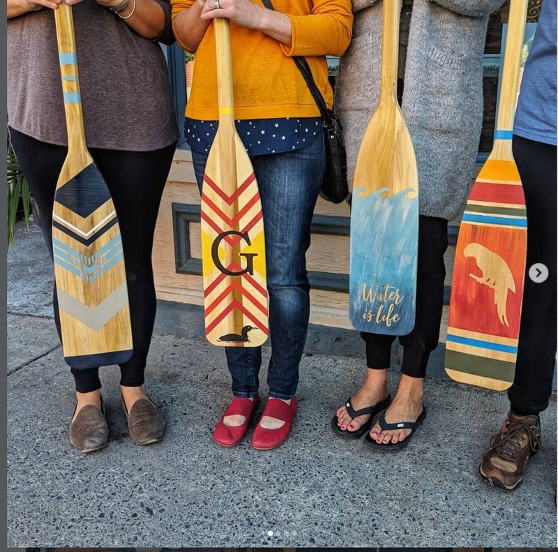 Customers holding hand-painted canoe paddles from a workshop